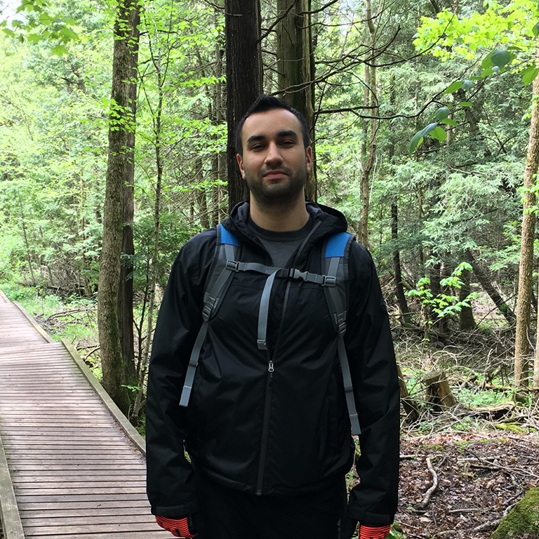 Julian, wearing a backpack, smiling on a hike in the woods